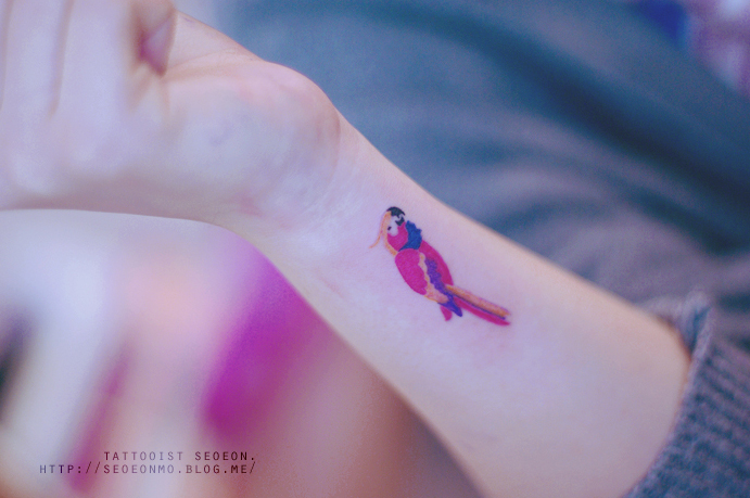 Minimalistic tattoo by Seoeon on wrist, featuring a small and discreet colorful bird design. Minimalistic tattoo by Seoeon on wrist, featuring a small and discreet colorful bird design.