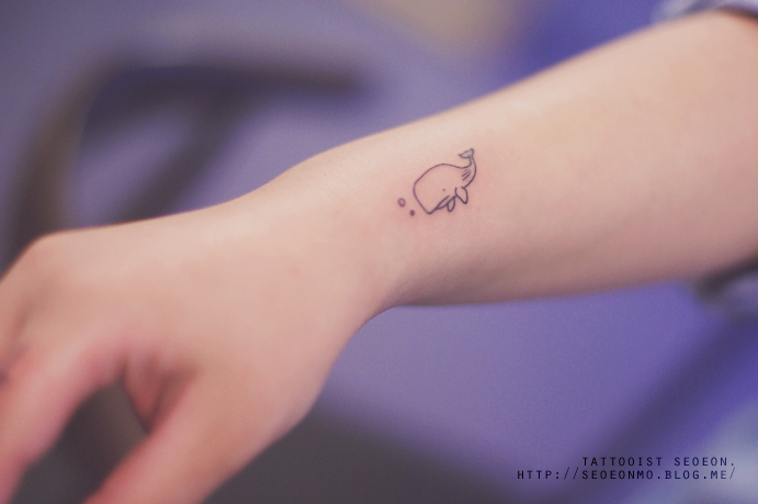 Minimalistic tattoo by Seoeon of a small whale on a wrist, showcasing a discreet and feminine design. Minimalistic tattoo by Seoeon of a small whale on a wrist, showcasing a discreet and feminine design.