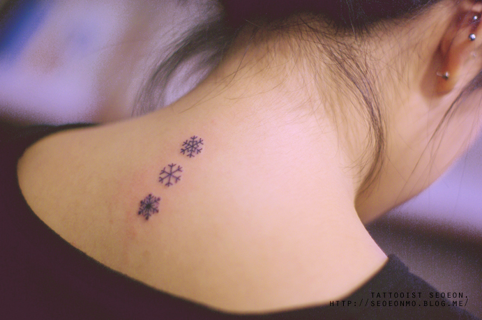 Minimalistic tattoo of small snowflakes on the back of a woman’s neck by Seoeon. Minimalistic tattoo of small snowflakes on the back of a woman’s neck by Seoeon.