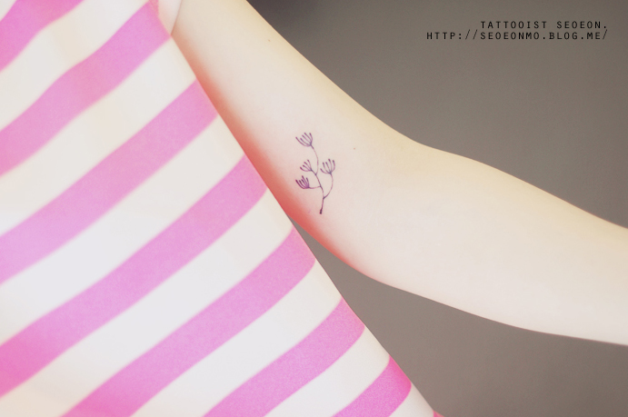 Minimalistic tattoo of a delicate flower on an arm by Seoeon, showcasing a feminine and discreet design. Minimalistic tattoo of a delicate flower on an arm by Seoeon, showcasing a feminine and discreet design.