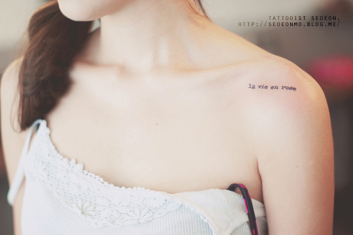 Minimalistic tattoo by Seoeon on woman's shoulder, featuring the phrase "la vie en rose. Minimalistic tattoo by Seoeon on woman's shoulder, featuring the phrase "la vie en rose.