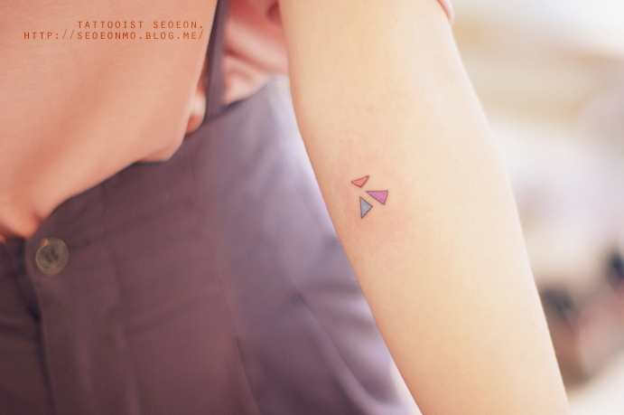 Minimalistic feminine tattoo by Seoeon, featuring small colorful geometric shapes on an arm. Minimalistic feminine tattoo by Seoeon, featuring small colorful geometric shapes on an arm.