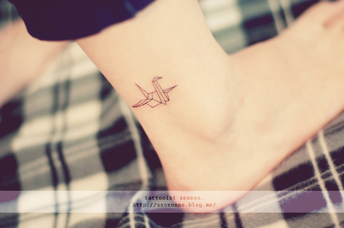 Minimalistic tattoo by Seoeon of an origami crane on an ankle, showcasing a discreet and feminine design. Minimalistic tattoo by Seoeon of an origami crane on an ankle, showcasing a discreet and feminine design.