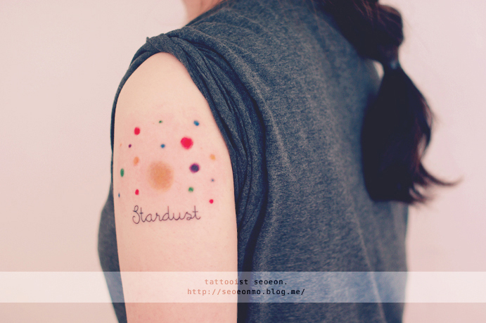 Minimalistic tattoo by Seoeon featuring colorful dots and the word "Stardust" on a person's arm. Minimalistic tattoo by Seoeon featuring colorful dots and the word "Stardust" on a person's arm.