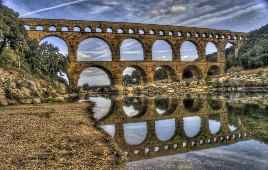 Ancient mystical bridge with multiple arches reflecting in calm river water surrounded by lush greenery.