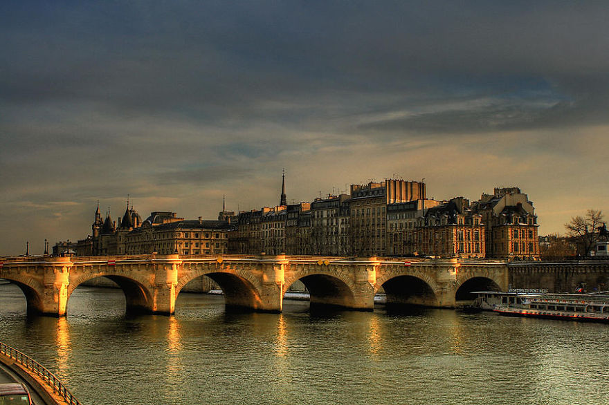 Stone bridge over calm river at sunset with historic buildings in the background, showcasing mystical bridges and serene atmosphere.