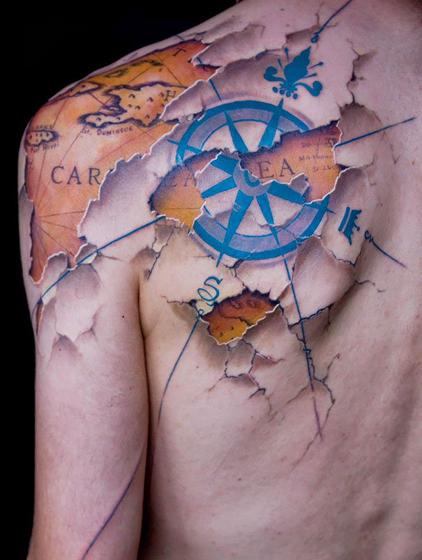 3D tattoo of a torn map and compass on a shoulder, showcasing intricate details and vibrant colors.