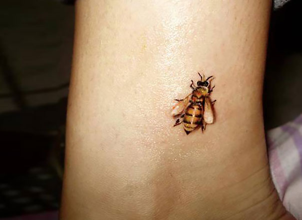 3D tattoo of a realistic bee on a person's ankle.