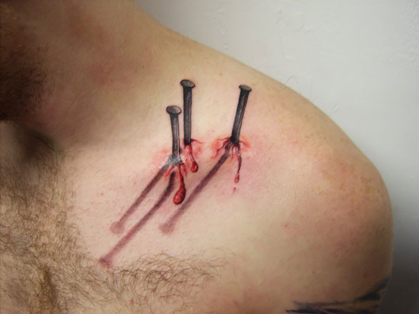 3D tattoo of realistic nails with shadows and blood effect on a person's shoulder.