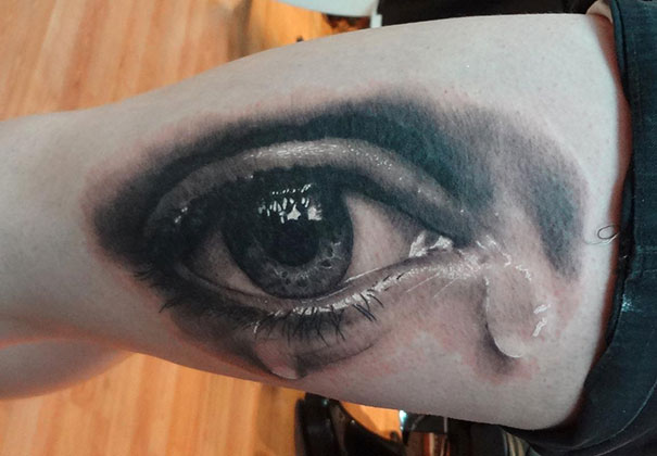 A mind-twisting 3D tattoo of a realistic eye with tear detail on an arm.