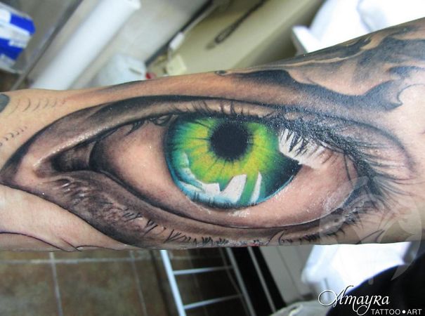 Close-up of a crazy 3D tattoo of a realistic green eye on an arm.