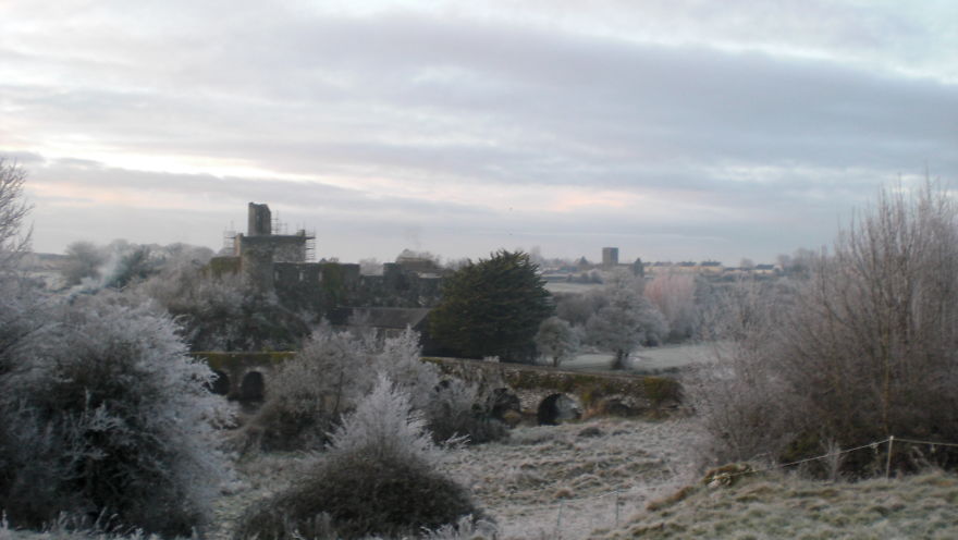 Frost-covered mystical stone bridge and castle ruins in a foggy landscape during early morning winter.