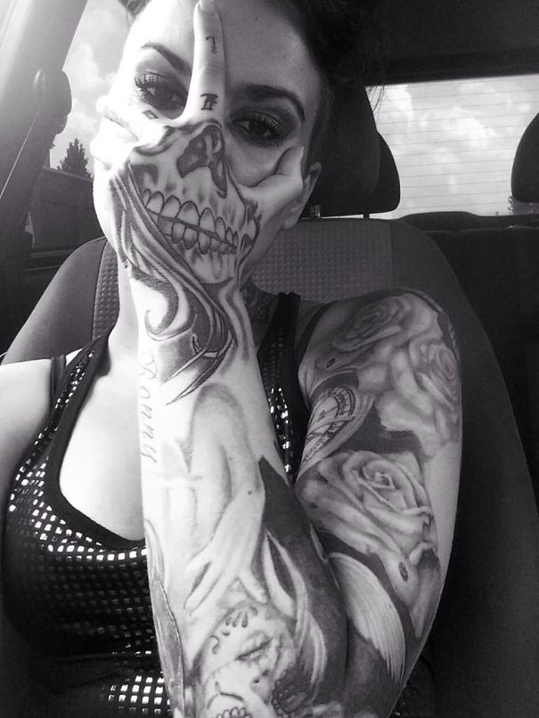 Close-up of a person with a detailed 3D skull tattoo on their hand, holding it over half their face.