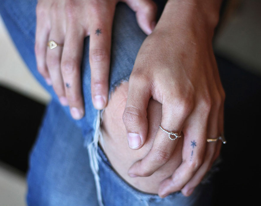 Hands with minimalist star tattoos, wearing silver rings and resting on ripped jeans. Hands with minimalist star tattoos, wearing silver rings and resting on ripped jeans.