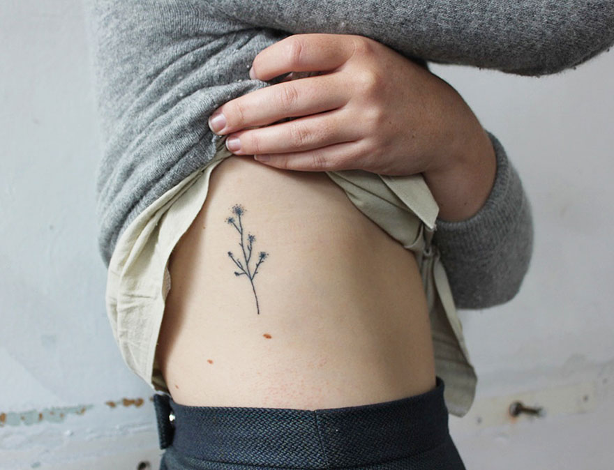Minimalist tattoo of a small branch on a person's side, showcasing artist's unique ink style. Minimalist tattoo of a small branch on a person's side, showcasing artist's unique ink style.