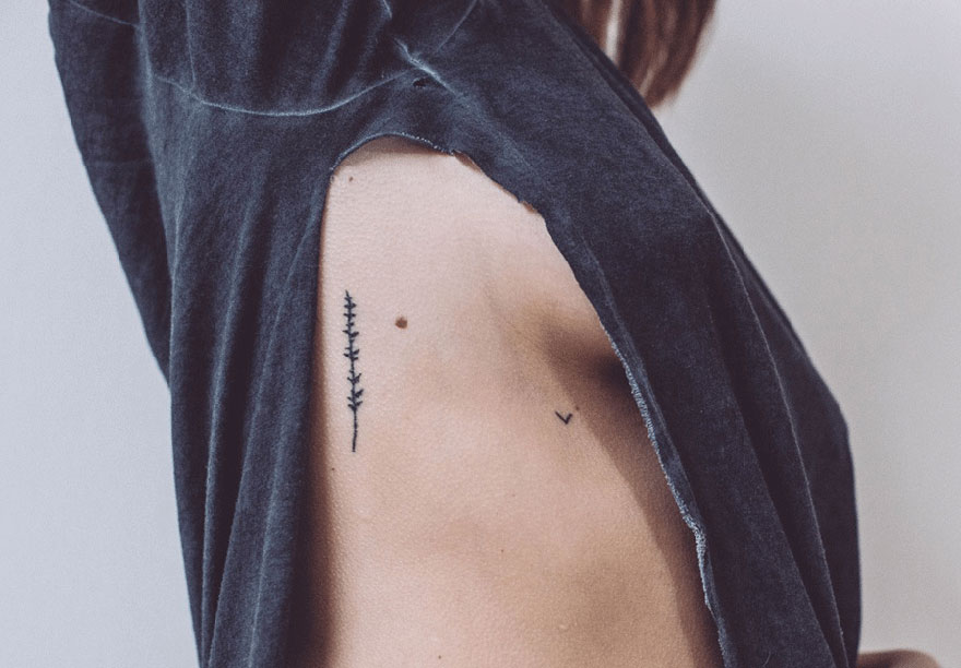 Minimalist tattoo of a plant and symbol inked on a person's side, showcasing tiny homemade art by a tattoo artist.