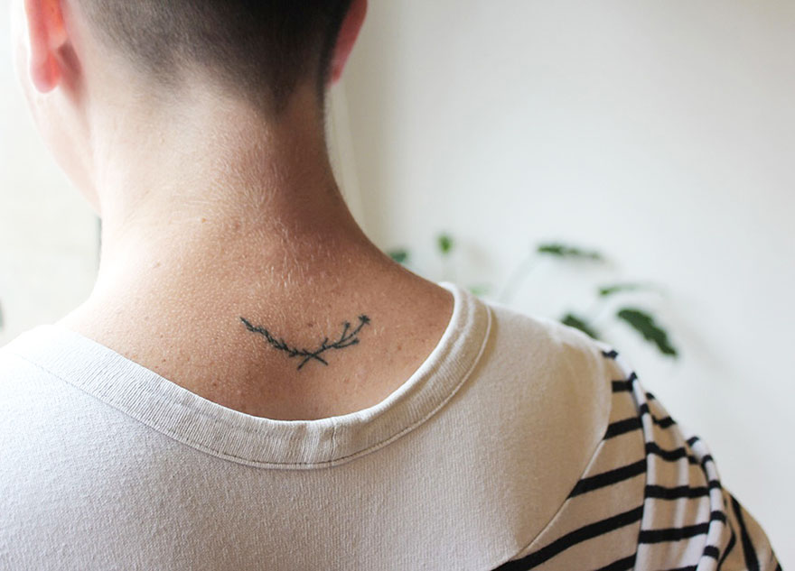 Minimalist tattoo of branches on the back of a neck, inked by an artist in a casual home setting.