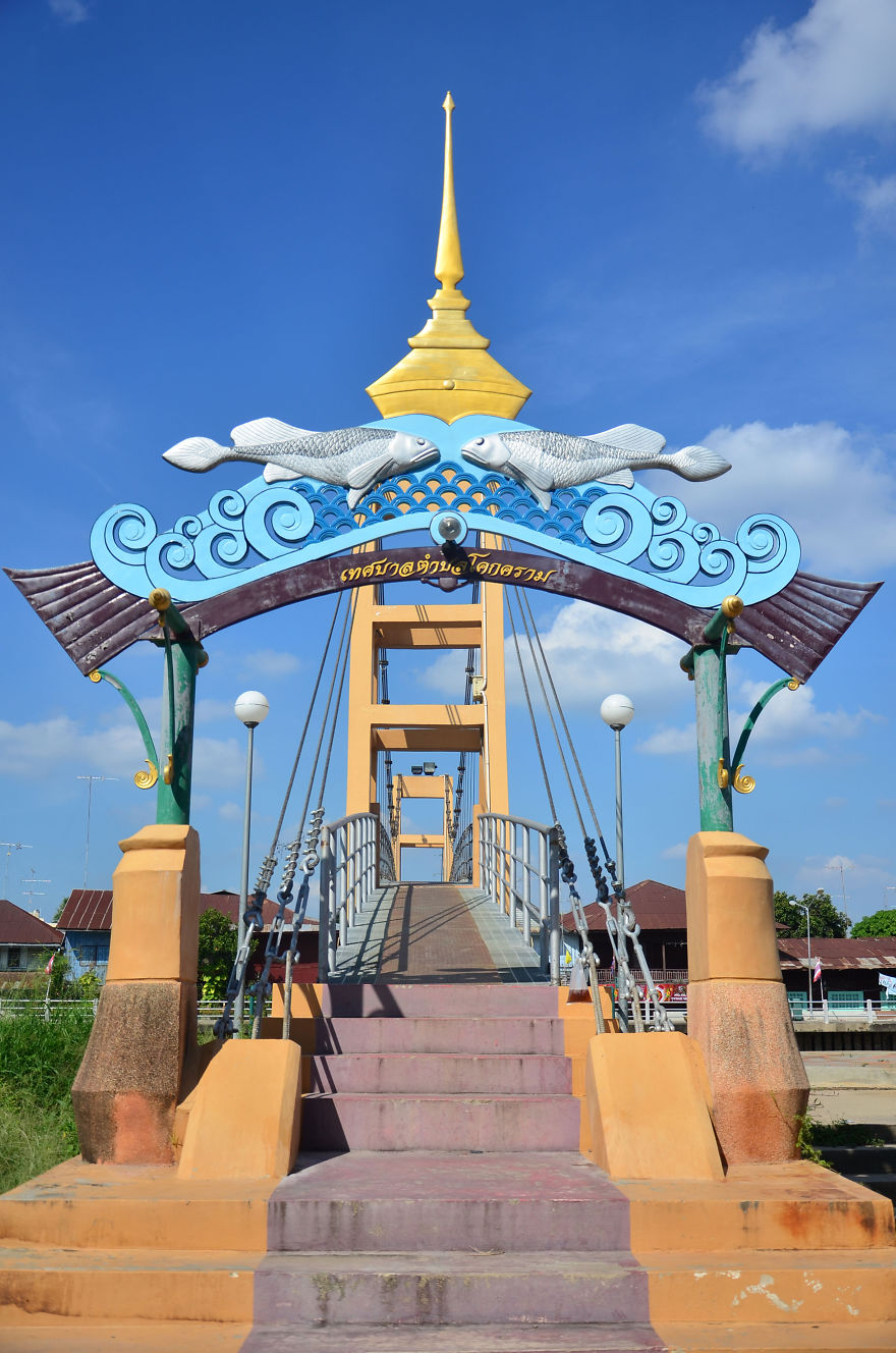 Mystical bridge entrance with colorful fish sculptures and decorative archway under a clear blue sky.