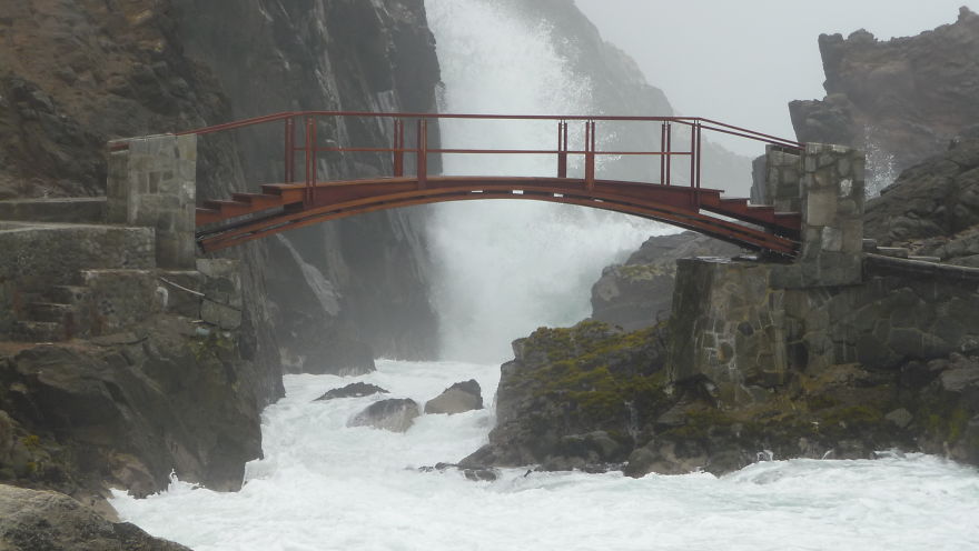 Mystical bridge over rocky waters with misty cliffs, creating an enchanting atmosphere in a remote natural setting.