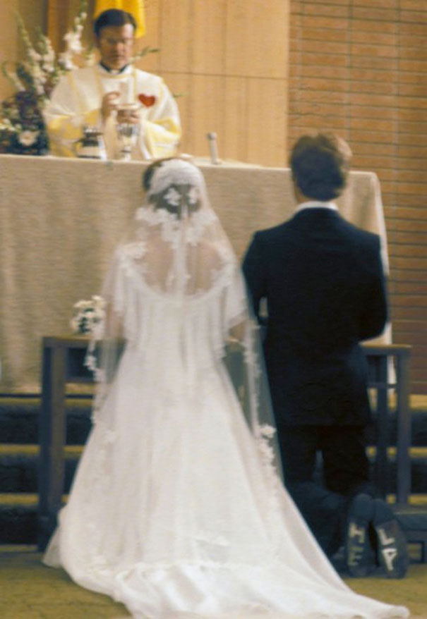 A bride and groom kneel at the altar during a wedding ceremony, with a hidden surprise visible on the groom's shoes.