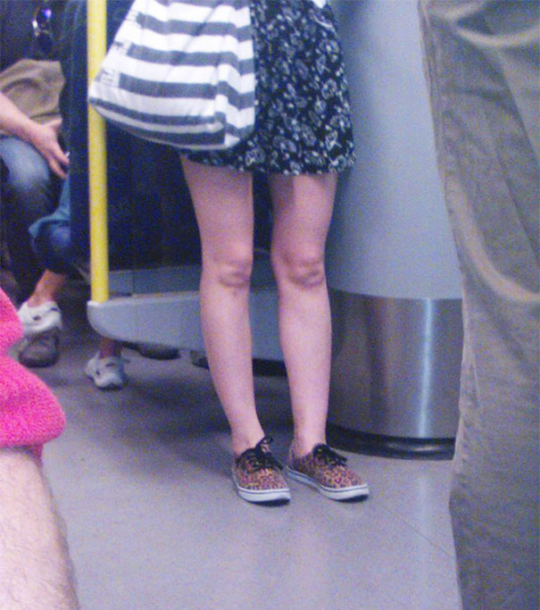 Woman standing on a subway with unique patterns on her shoes, creating a surprising visual effect.
