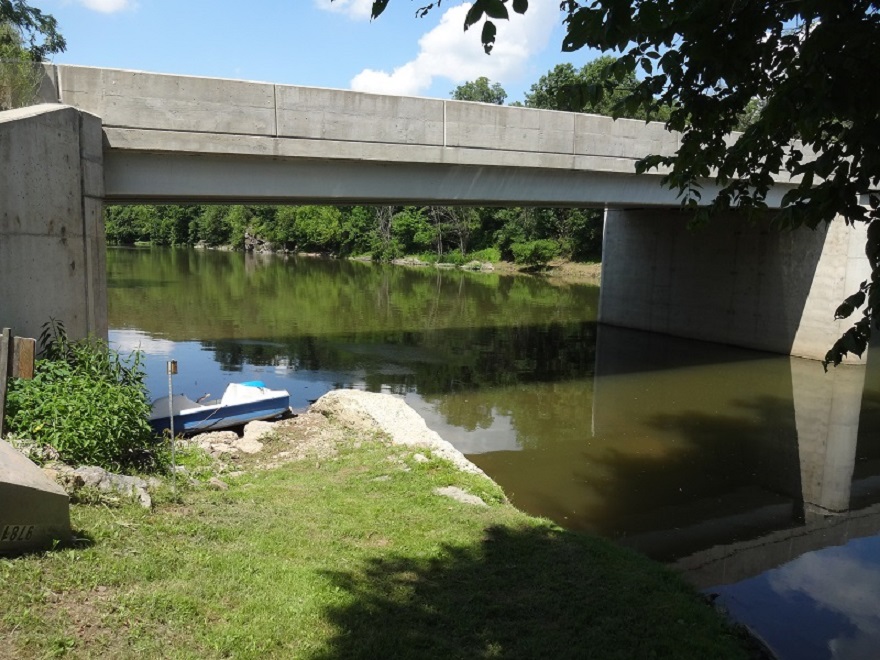 Concrete mystical bridge over calm river with green trees and blue sky reflecting in the water