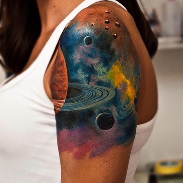 Colorful cosmic tattoo on arm featuring planets and nebula, perfect for astronomy lovers.