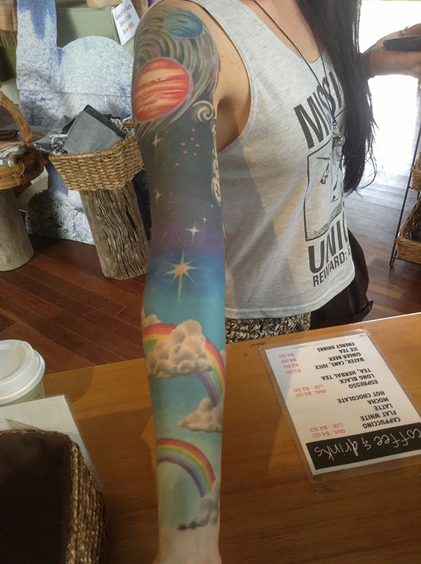 Colorful cosmic tattoo on arm featuring planets and a rainbow for astronomy lovers.