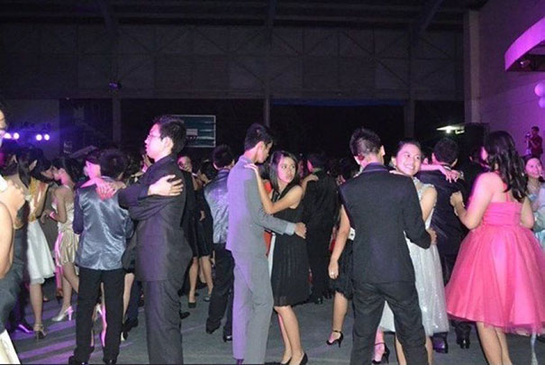 People dancing at a party in formal attire, with a surprising element in the background.