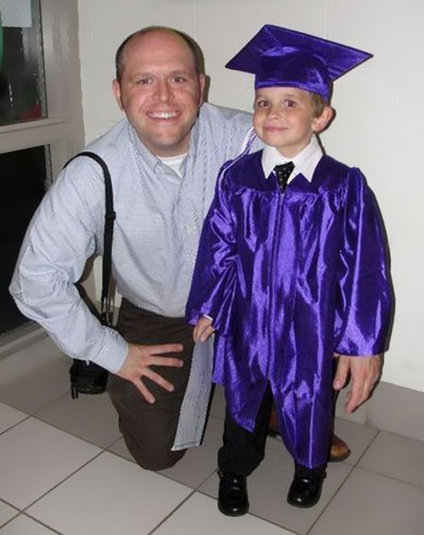 Man kneeling beside a child in a purple graduation gown and cap, both smiling.