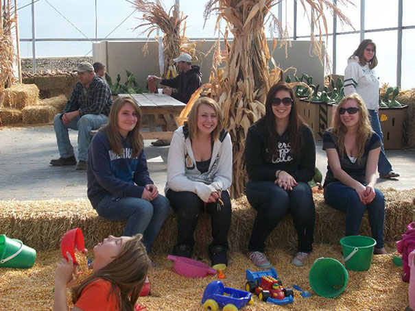 Group of women sitting on hay bales in a play area, with one child lying down among toys.