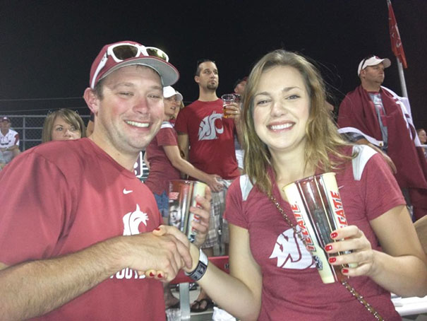Fans at a sports event holding drinks, with a surprising detail in the background.