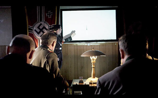 N**i officers in a dimly lit room, one pointing at a map on the wall.