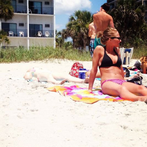 A woman sunbathing on a beach towel, with a surprising shadow effect on the sand.