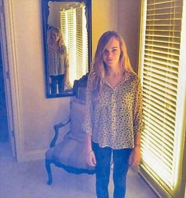A woman stands near a mirror with blinds in the background, creating an intriguing optical illusion effect.