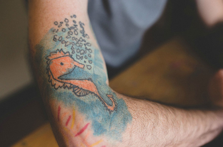 Father's arm with colorful seahorse tattoo based on son's drawing.
