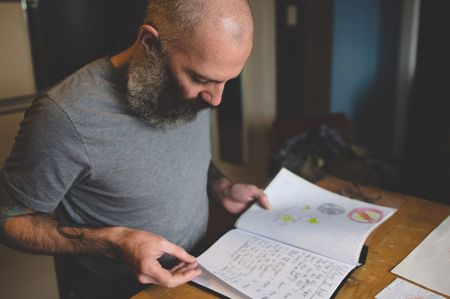 Dad reviews son's drawings, considering for tattoo on arm, part of his personal body art collection from son's childhood.