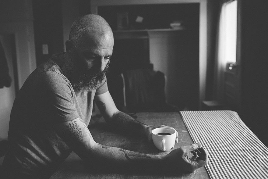 Man with tattoos holding a coffee cup, showcasing child&rsquo;s drawings on arm.