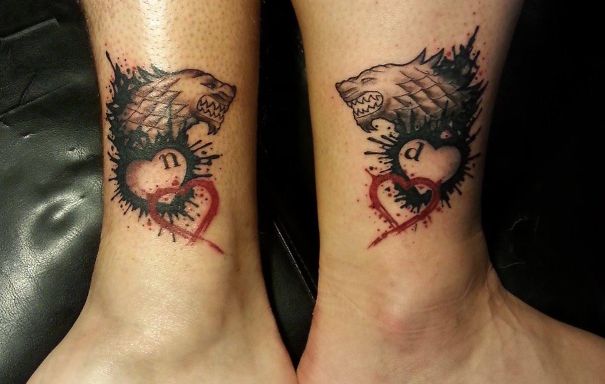 Matching couple tattoos of wolves and hearts on ankles.