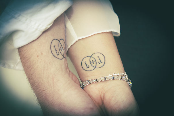 Matching couple tattoos with initials in overlapping circles on two wrists.