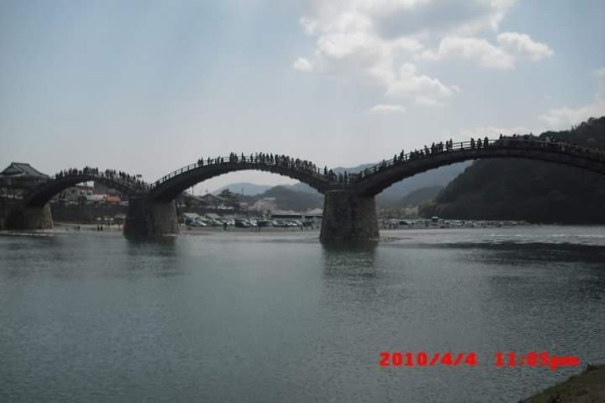 Stone arch bridge over calm water with people walking, creating a mystical bridge scene in a serene landscape.