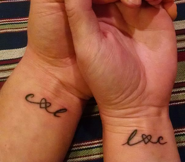 Matching couple tattoos on wrists with intertwined heart and letters.