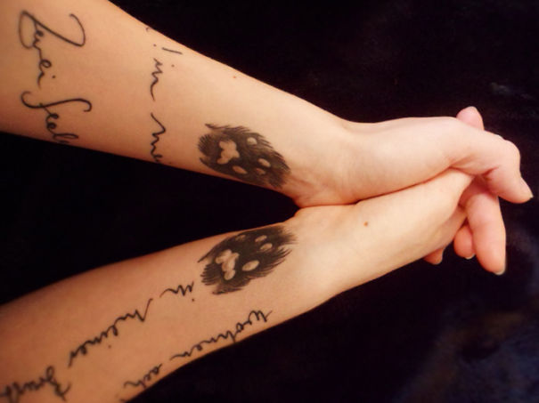 Couple holding hands, displaying matching tattoos with text and heart-shaped designs on their forearms.