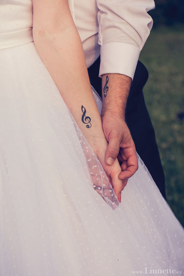 Couple holding hands, displaying matching music note tattoos on their wrists, symbolizing love and unity.