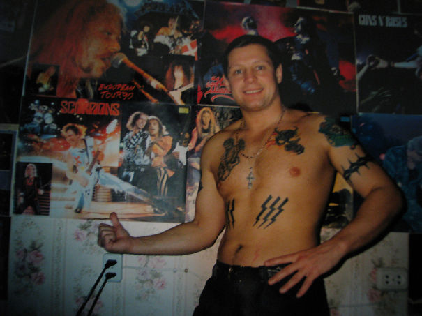Shirtless senior with tattoos in a room of band posters, showcasing how ink looks over time.