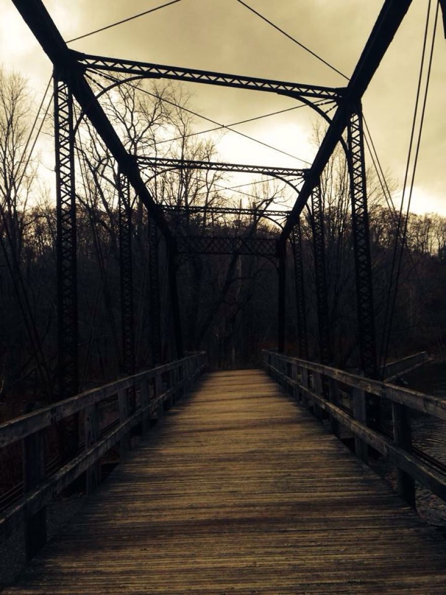 Old wooden mystical bridge with iron framework crossing a river surrounded by bare trees under a cloudy sky