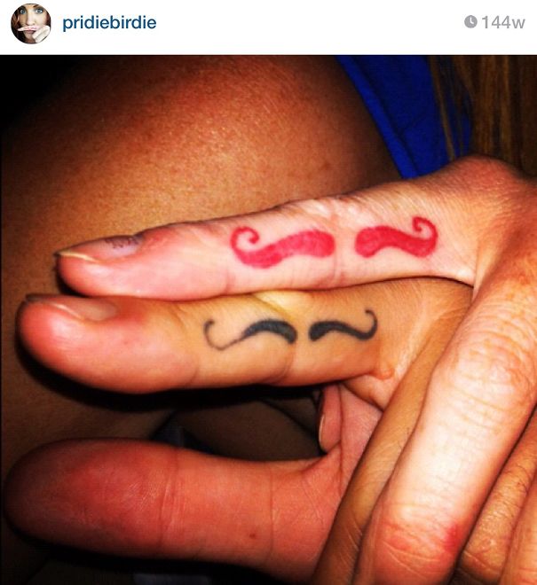 Matching couple tattoos with red and black mustaches on fingers.