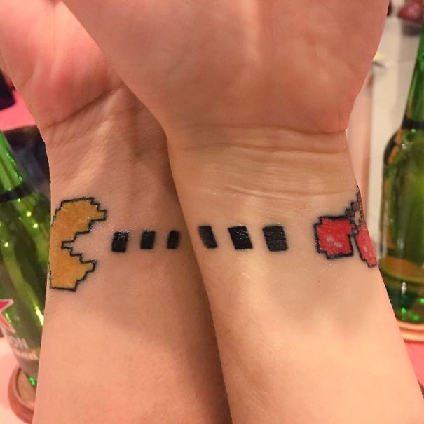 Matching couple tattoos featuring a pixelated game character design on wrists.