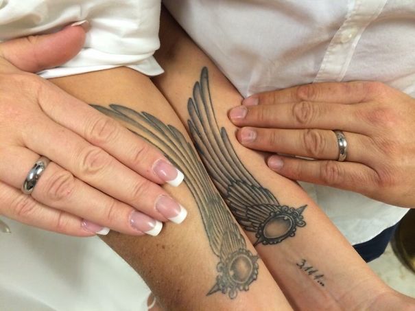 Matching couple tattoos of angel wings on forearms, symbolizing lovers growing old together, with hands gently resting on them.