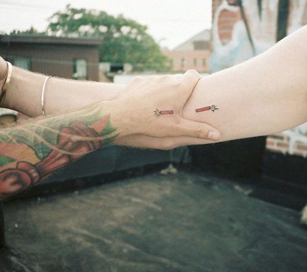 Couple holding hands with matching tattoos of a lit firecracker, symbolizing enduring love.